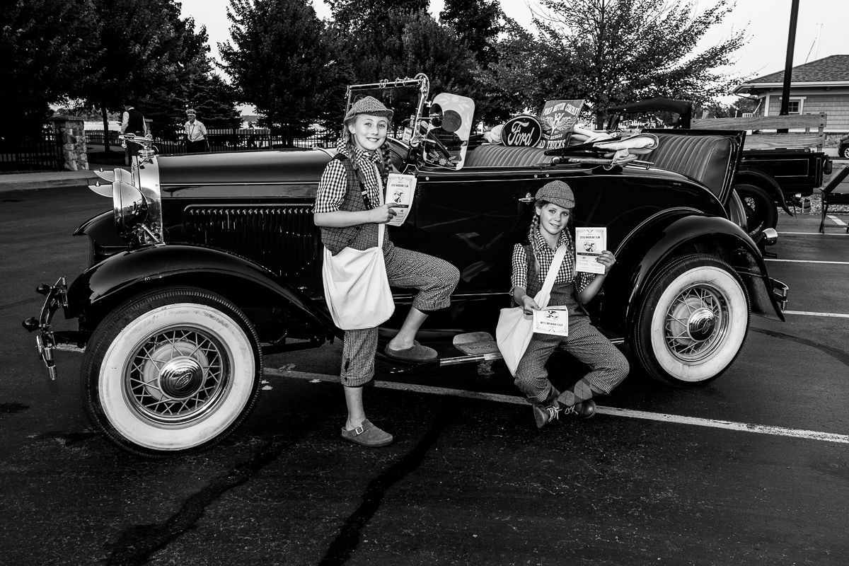 Two people are standing next to an old car in a parking lot.
