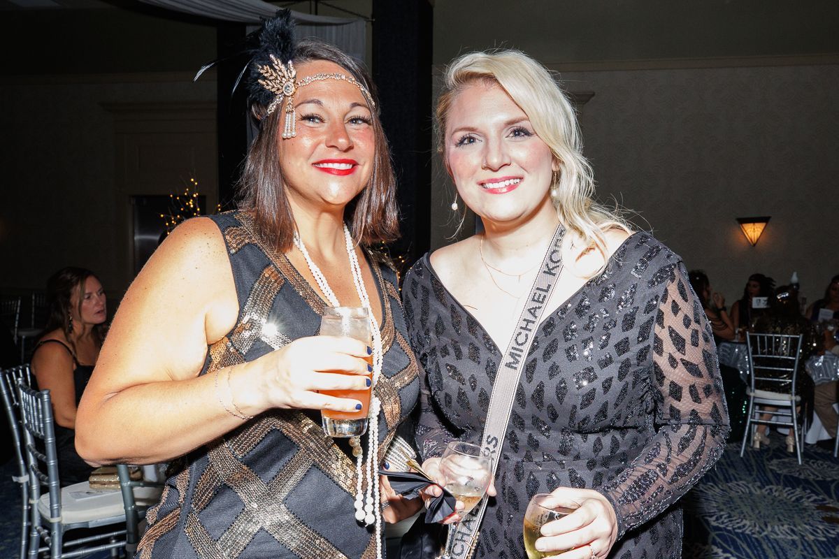 Two women are posing for a picture at a party while holding drinks.