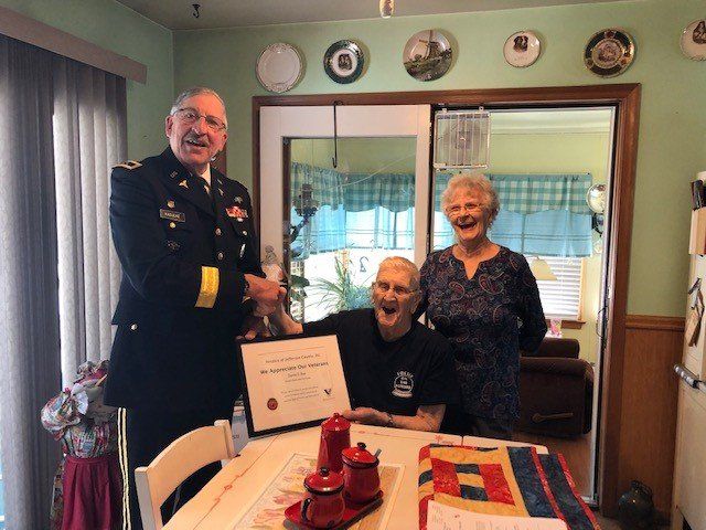 A man in a military uniform is giving a certificate to a man sitting at a table.