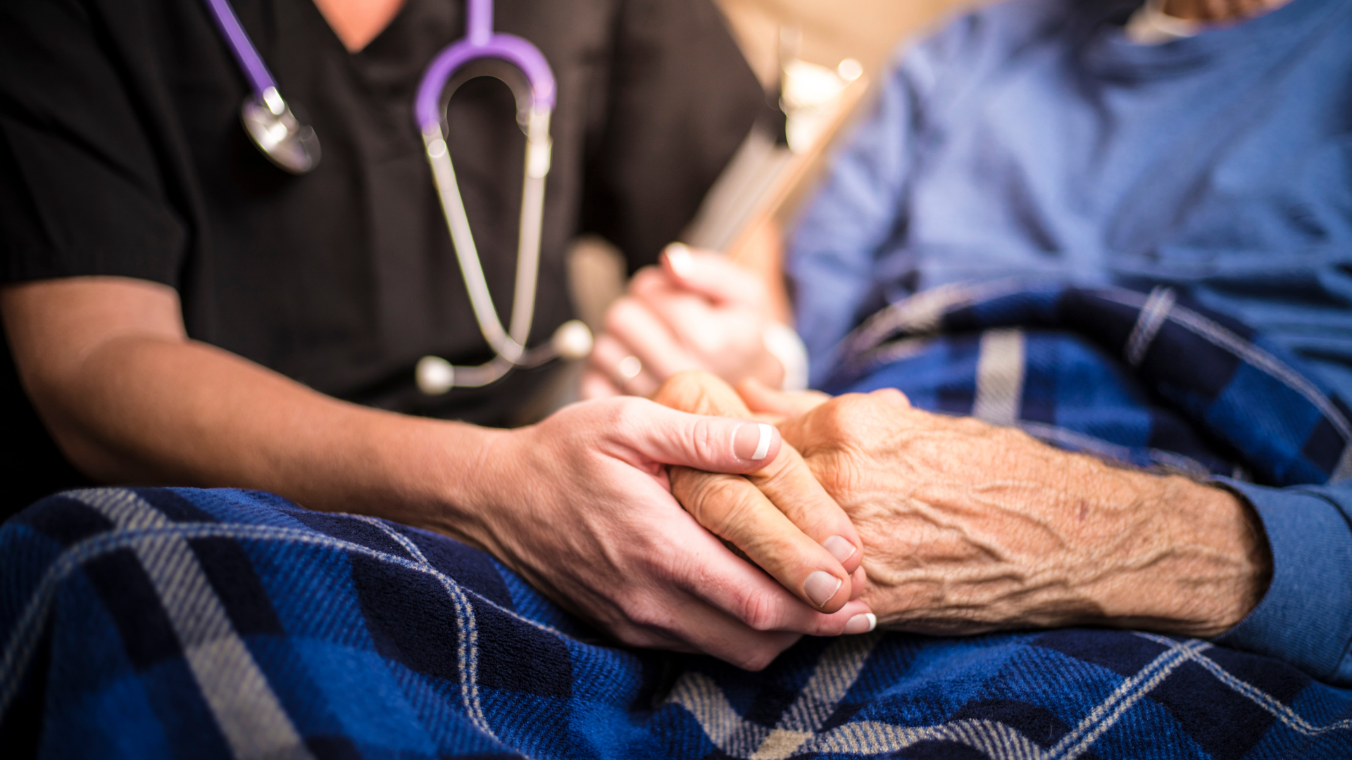 A nurse is holding the hand of an elderly man in a hospital bed.