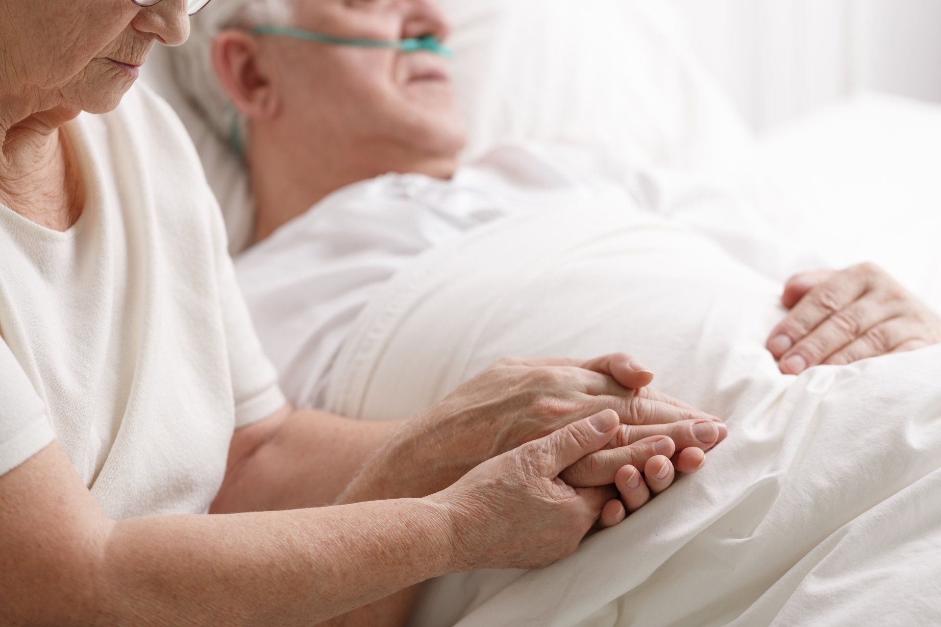 A woman is holding the hand of an elderly man in a hospital bed.