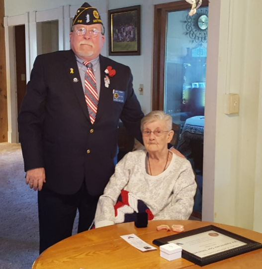 A man in a suit stands next to a woman sitting at a table