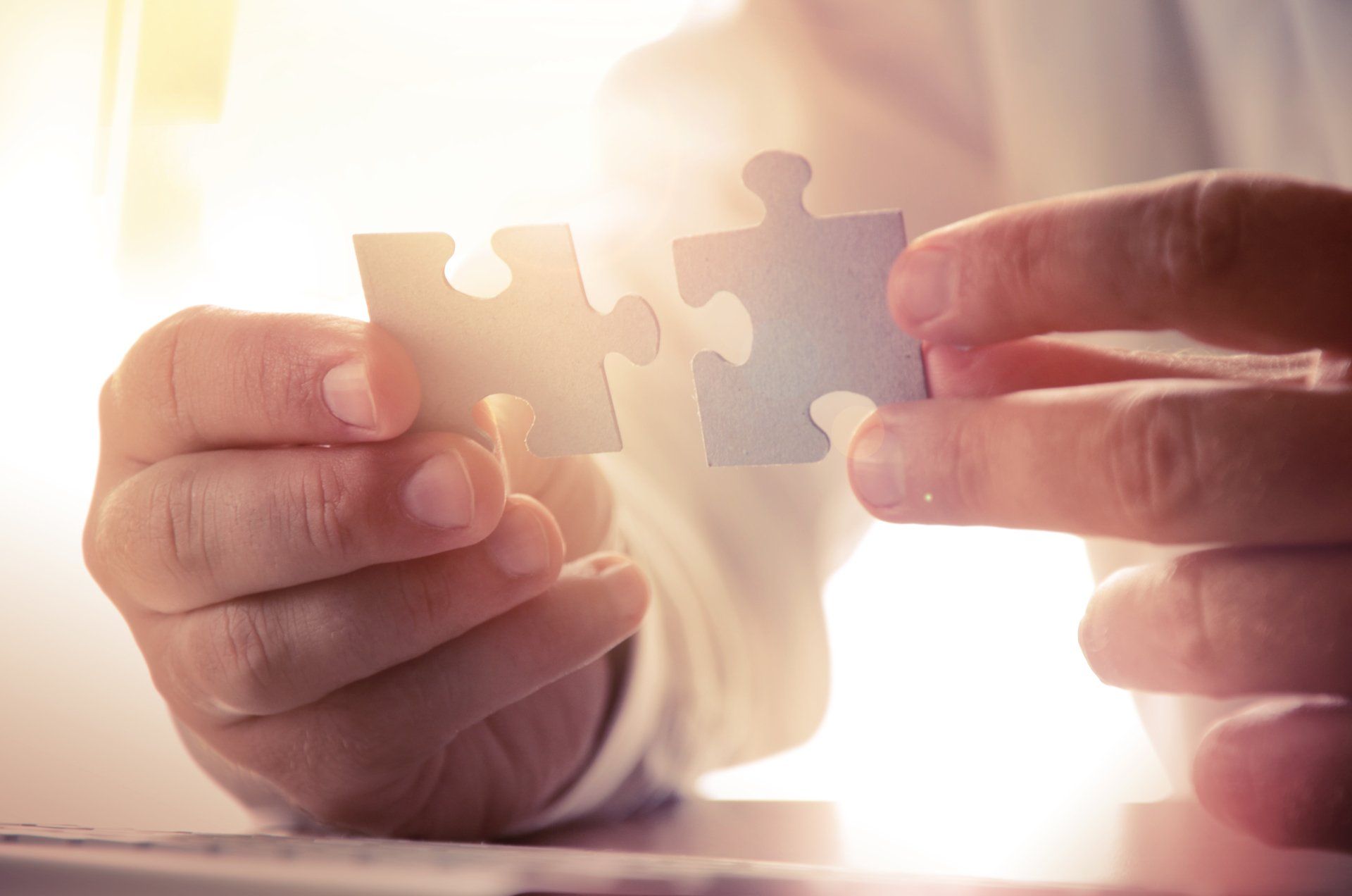 Hands holding two puzzle pieces, about to connect.