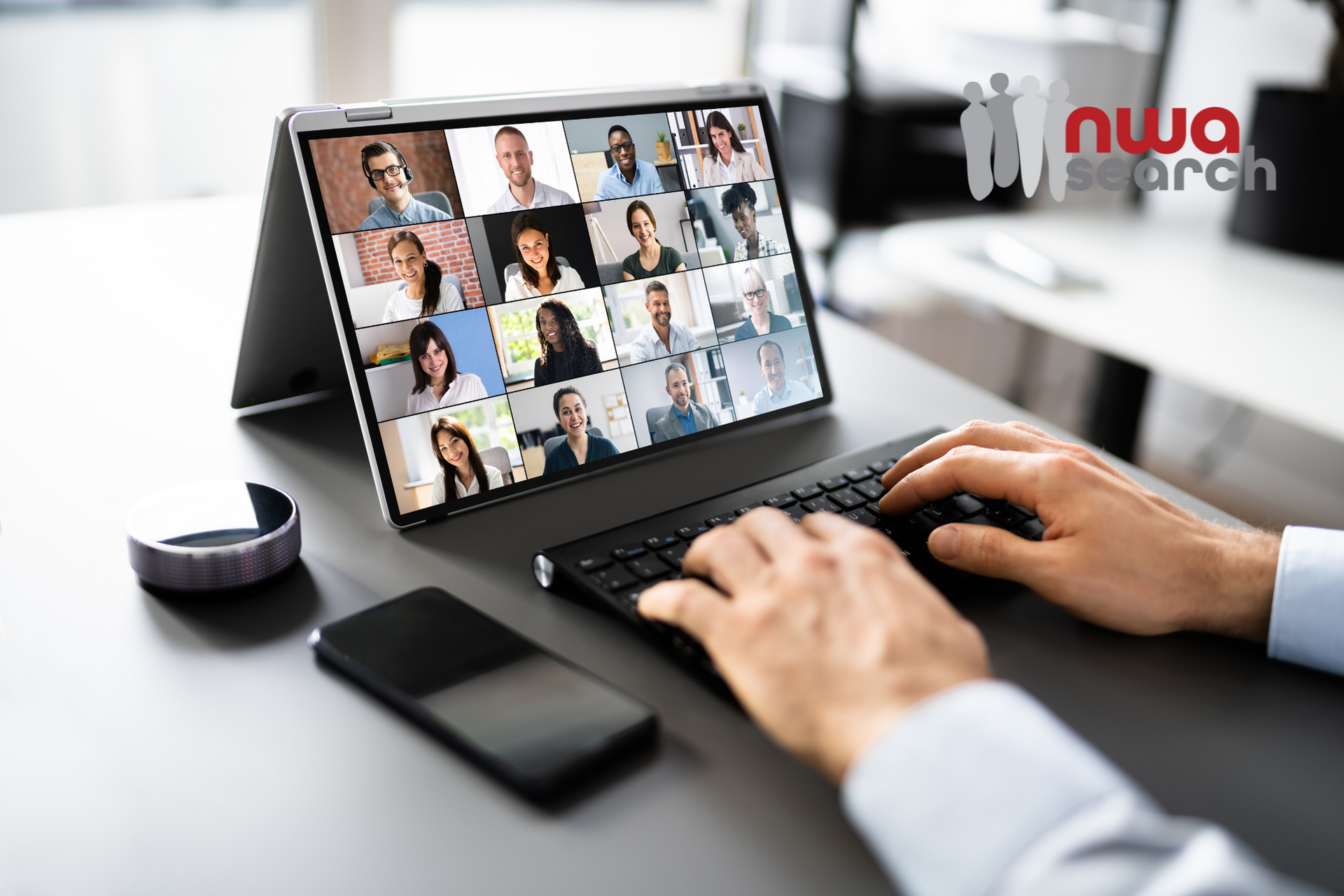 A person is typing on a laptop with a group of people on the screen remote working