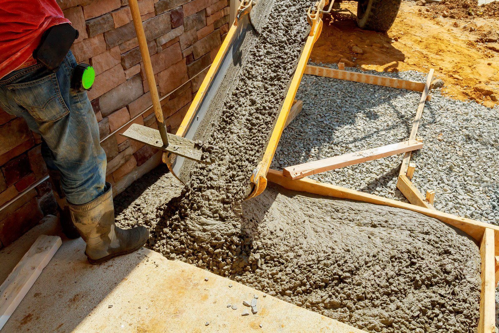 Worker pouring wet concrete into a wooden form for a sidewalk.