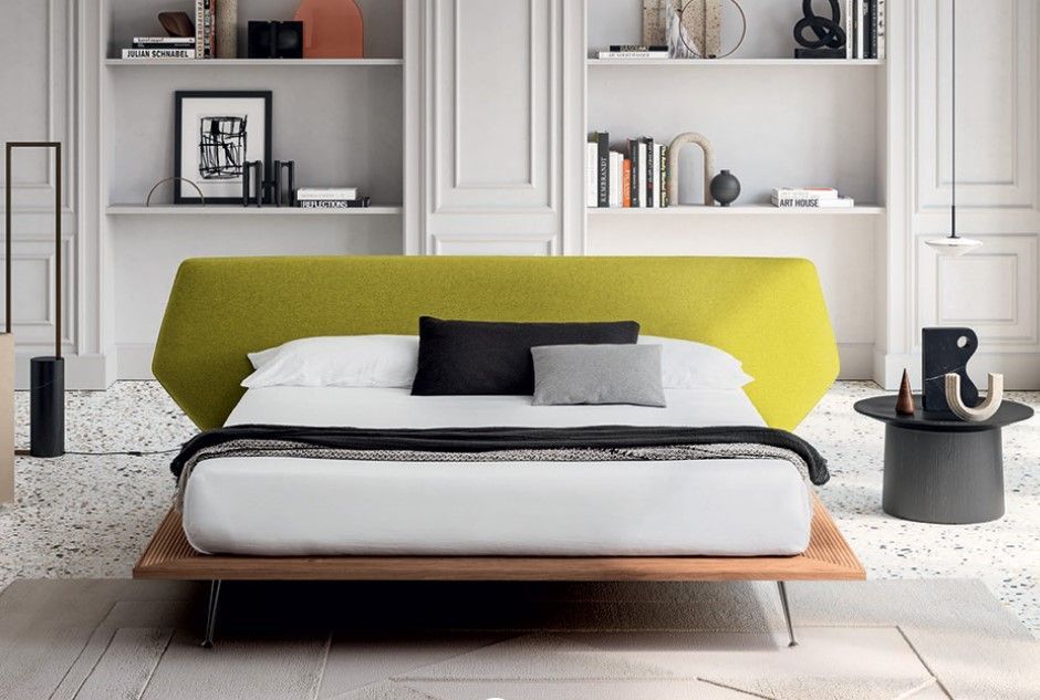 In un soggiorno c'è un letto con la testiera verde e lenzuola bianche.