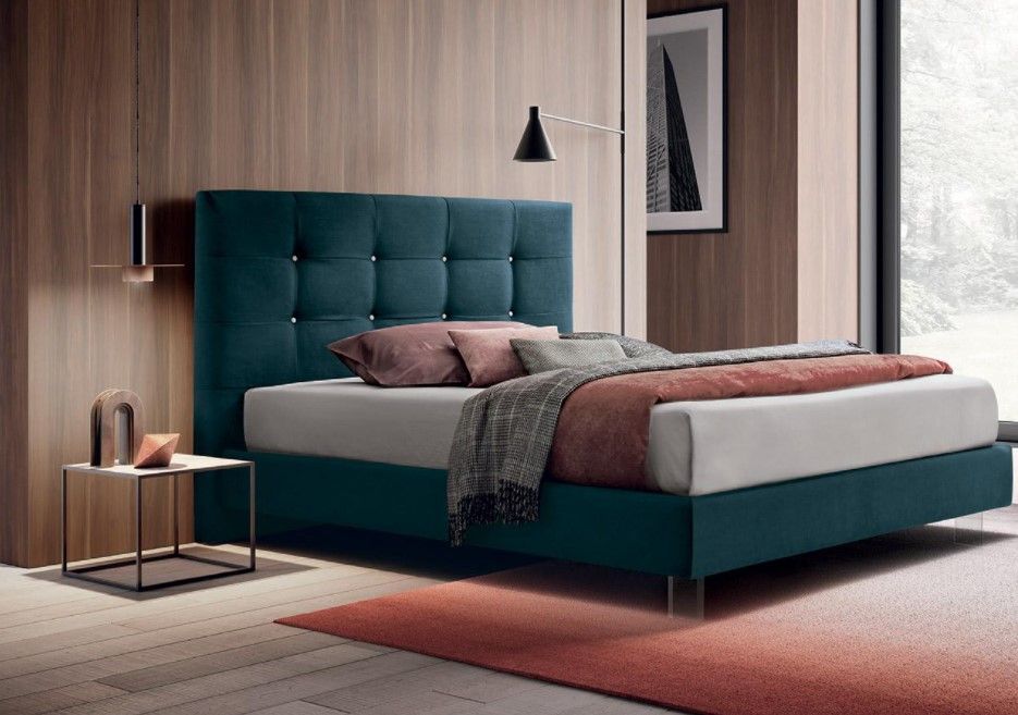 In una camera da letto, accanto a una finestra, c'è un letto con la testiera blu.