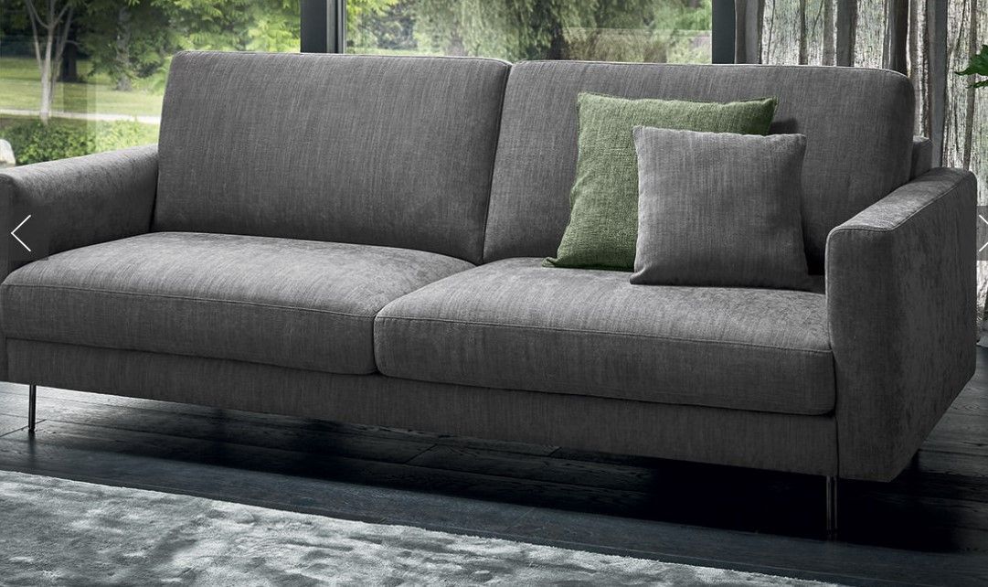 Un divano grigio con cuscini verdi è posizionato nel soggiorno, accanto a una finestra.