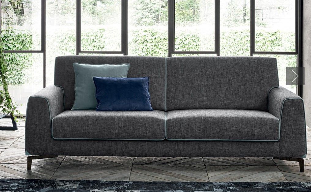 Un divano grigio con due cuscini è posizionato davanti a una finestra in un soggiorno.