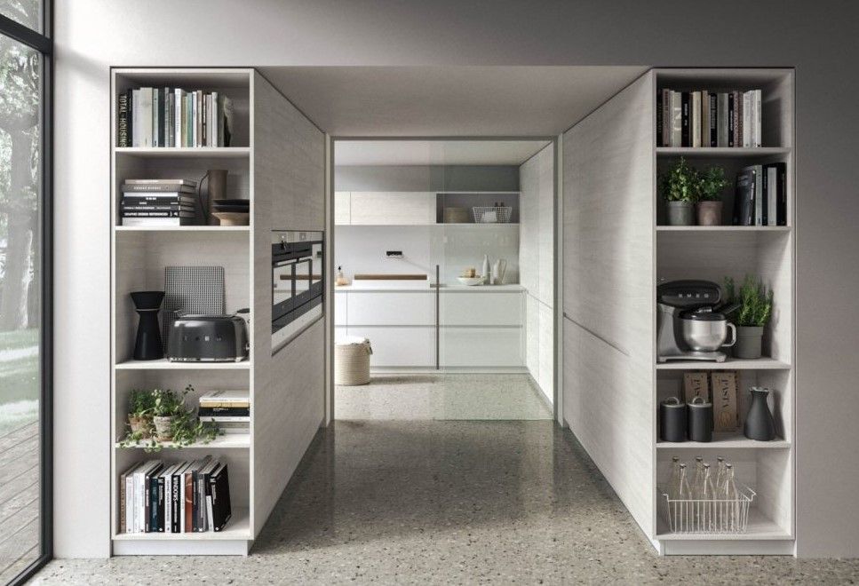 Un corridoio che conduce a una cucina con mobili e scaffali bianchi.