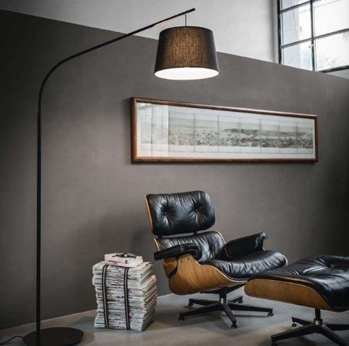 Un soggiorno con una sedia, un pouf, una lampada e un quadro sulla parete.