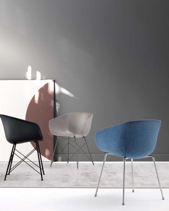 Tre sedie sono appoggiate su un tappeto davanti a un muro grigio.