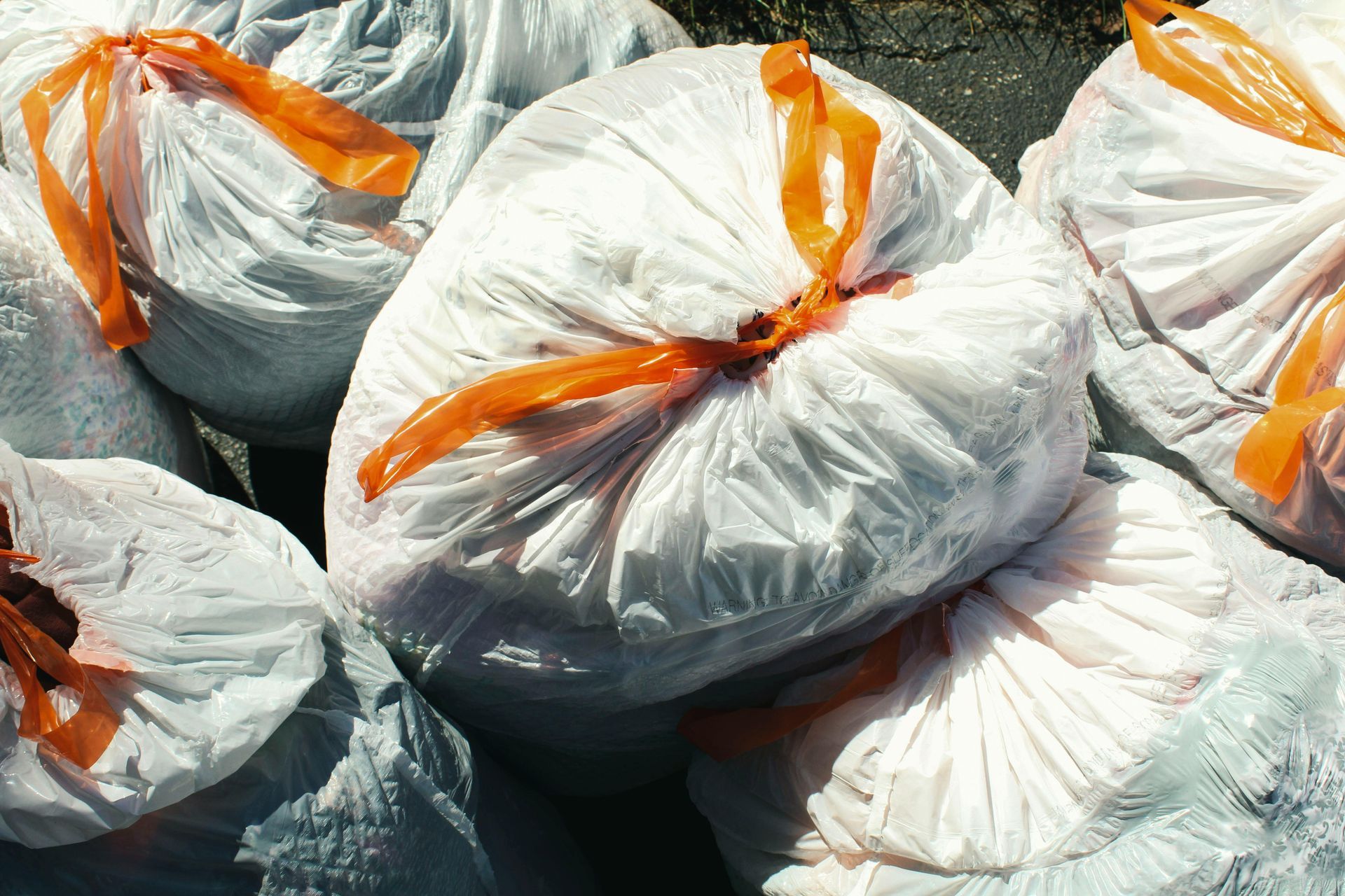 Several white plastic bags tightly tied with orange drawstrings, grouped together outdoors.