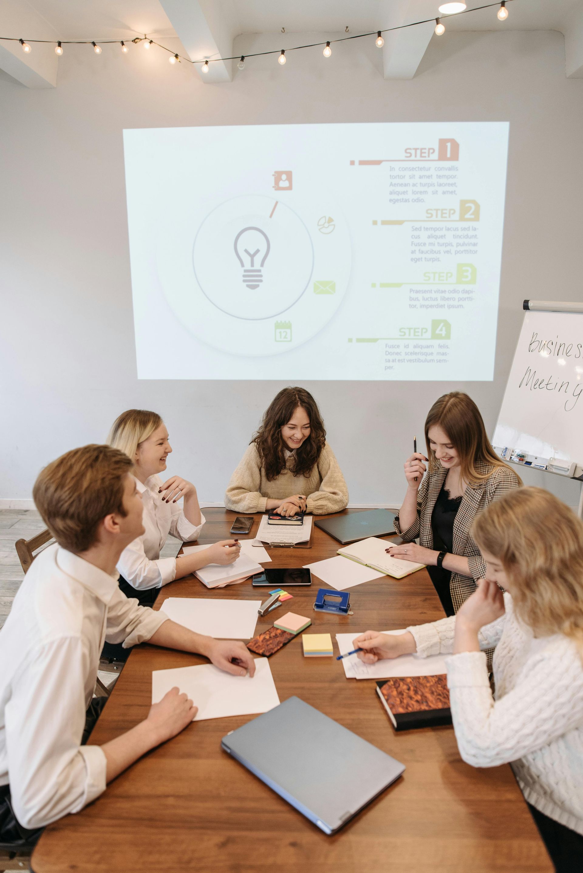A group of people are sitting around a table in front of a projector screen.