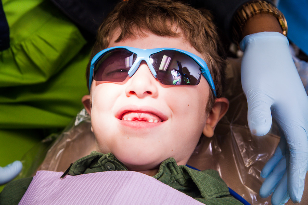 Little kid missing two front teeth smiling with glasses on in patient chair