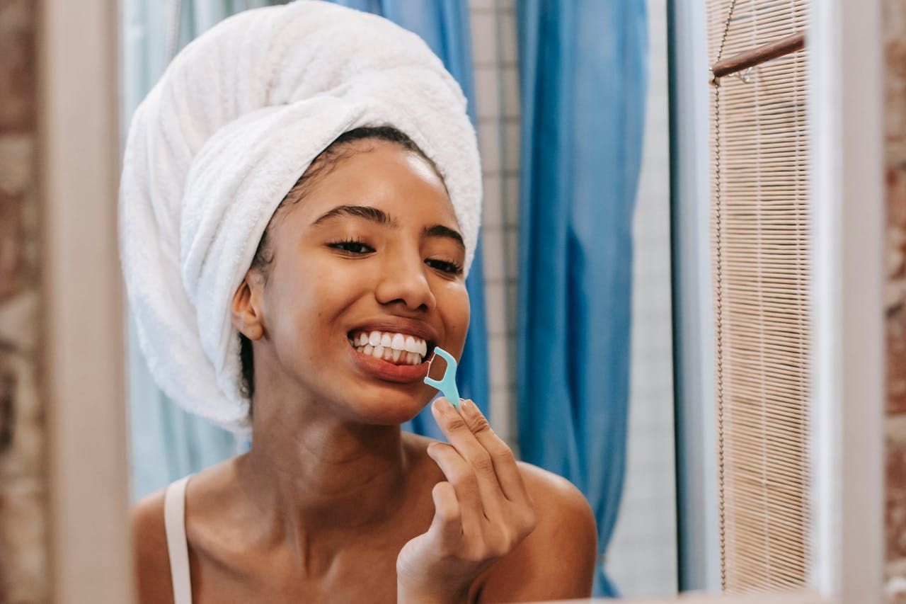 A woman with a towel wrapped around her head is brushing her teeth in front of a mirror.