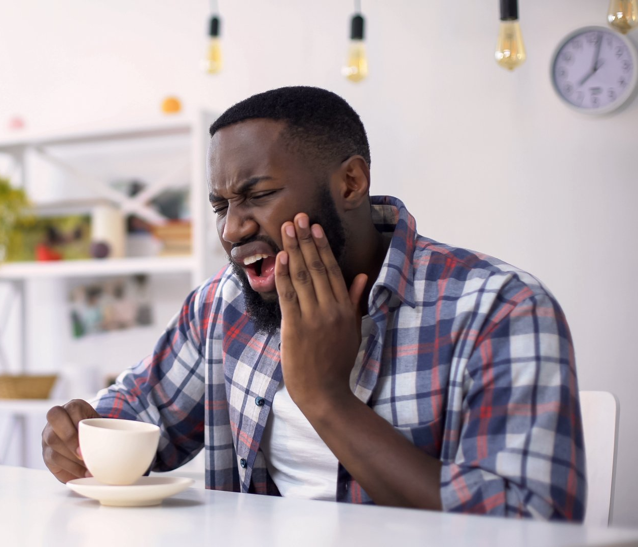 A man sitting with a cup of coffee is having tooth pain.