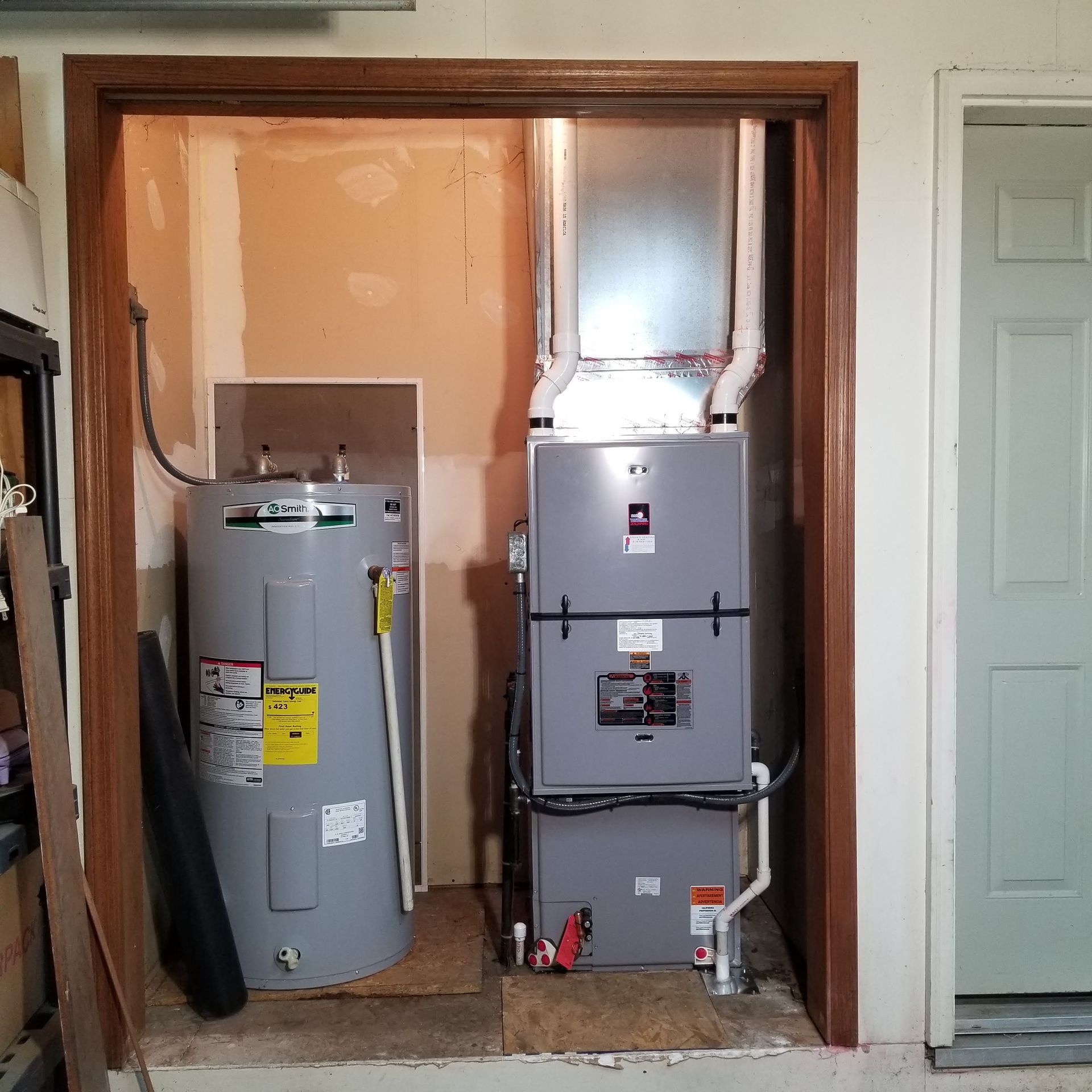 Water heater and furnace installed in a utility closet with a door on the right.