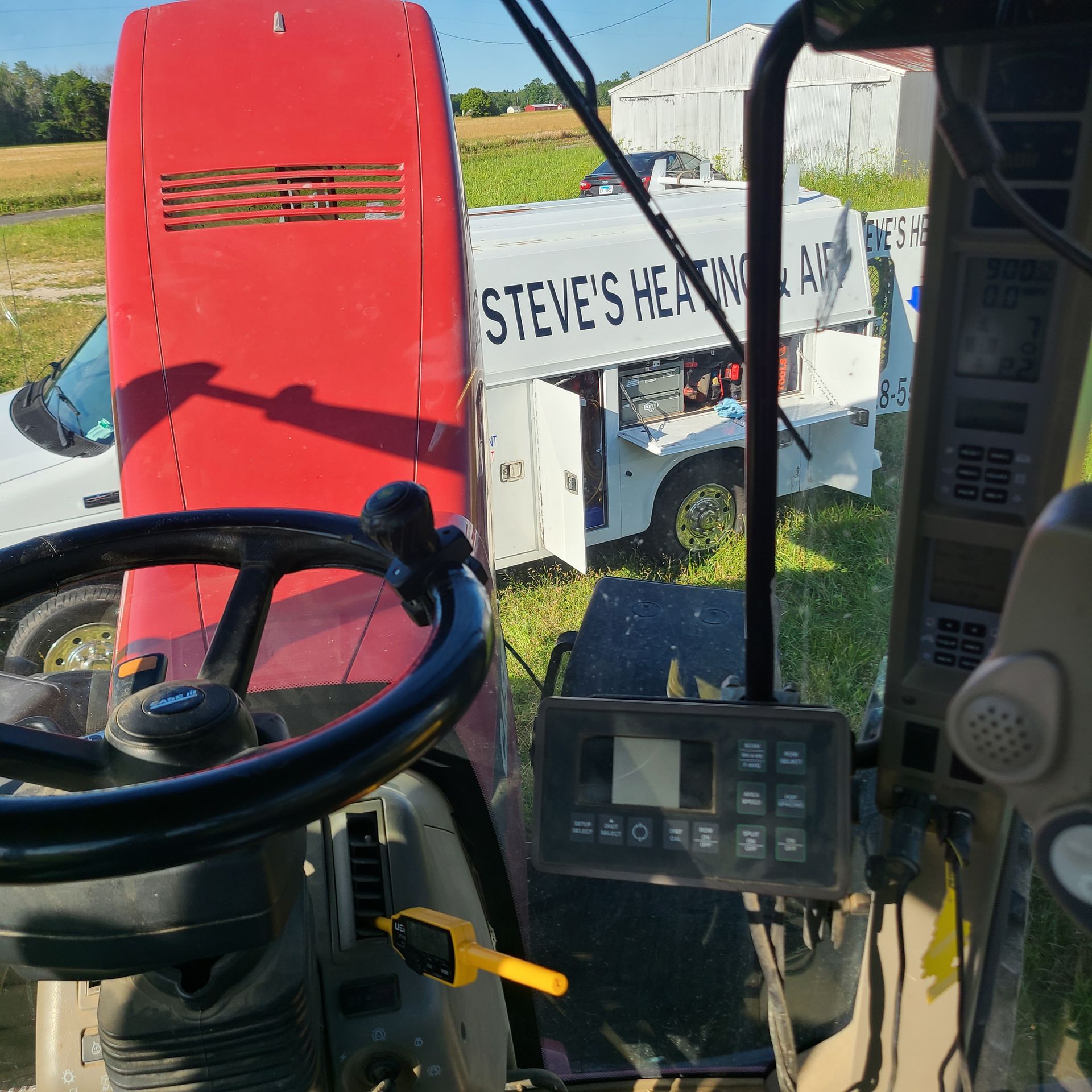 View from inside a tractor, red equipment, and a white work truck labeled 