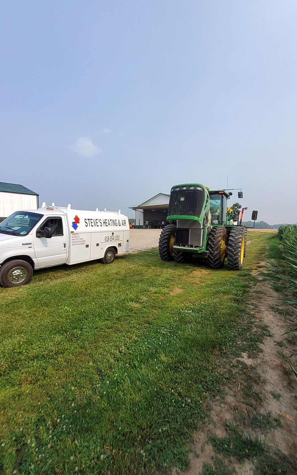White truck and green tractor on a grassy rural road, near buildings. Sunny day.