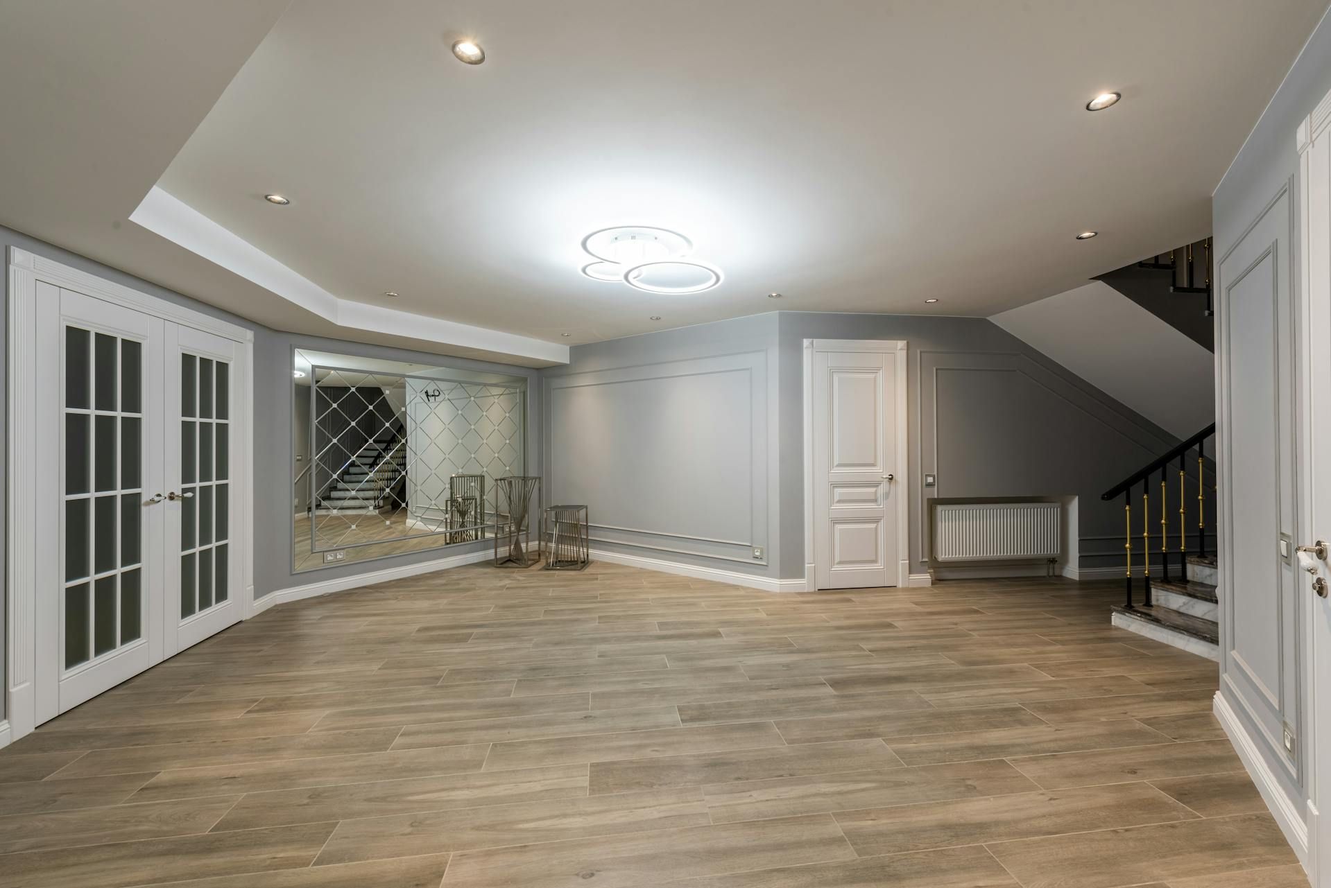 Empty modern living room with wood floors, gray walls, recessed lighting, and French doors