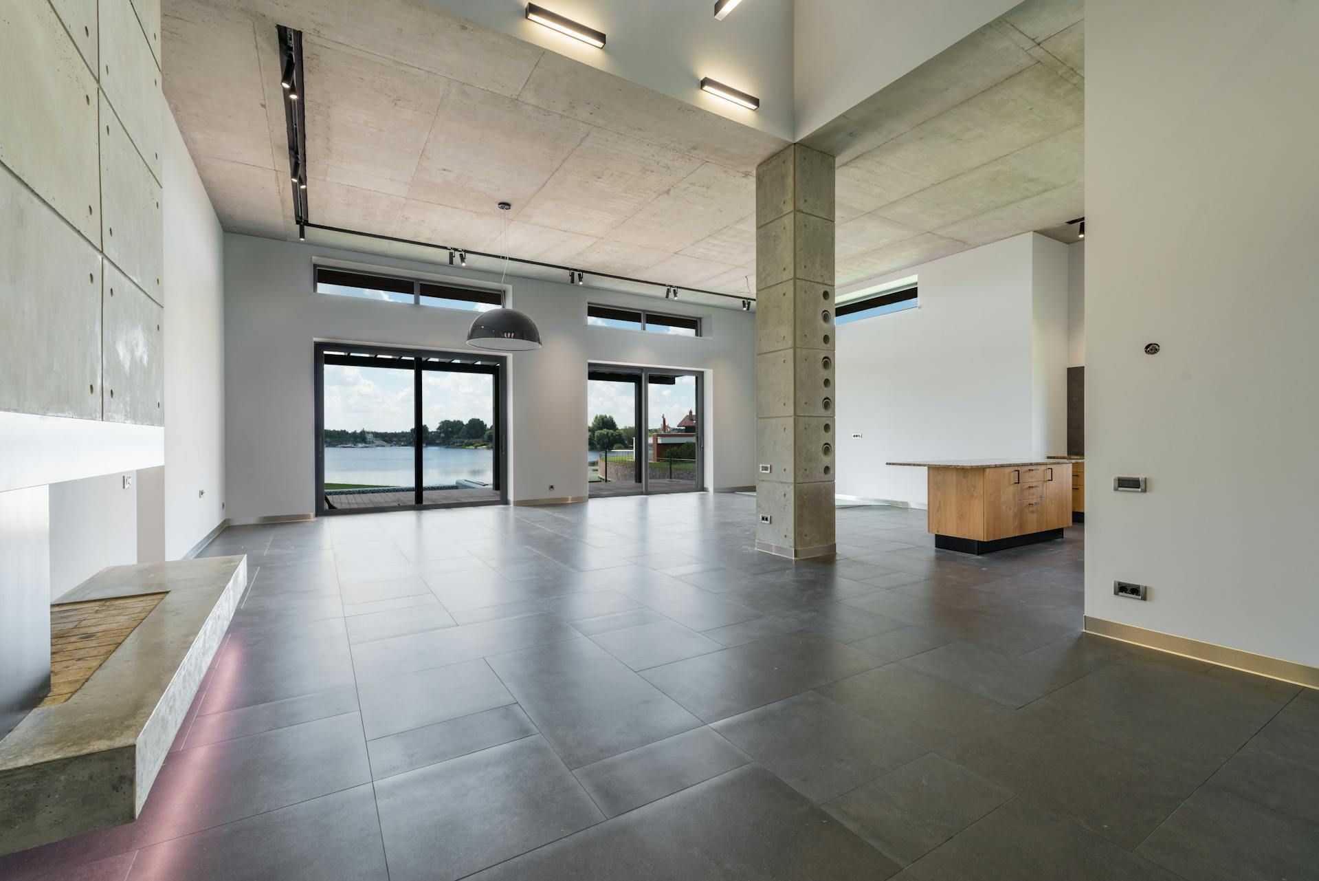 Empty modern loft interior with concrete floors, tall windows, and a central support column.