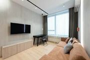 Modern living room with wall-mounted TV, desk, sofa, and large window with curtains