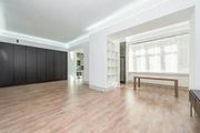 Bright empty modern room with light wood floors, white walls, black cabinets, and a long table by a window