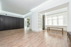 Bright empty modern room with light wood floors, white walls, black cabinets, and a long table by a window