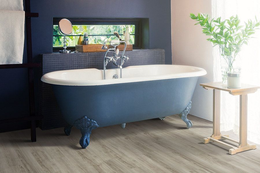 Blue clawfoot bathtub in a bright bathroom beside a small plant on a wooden stand