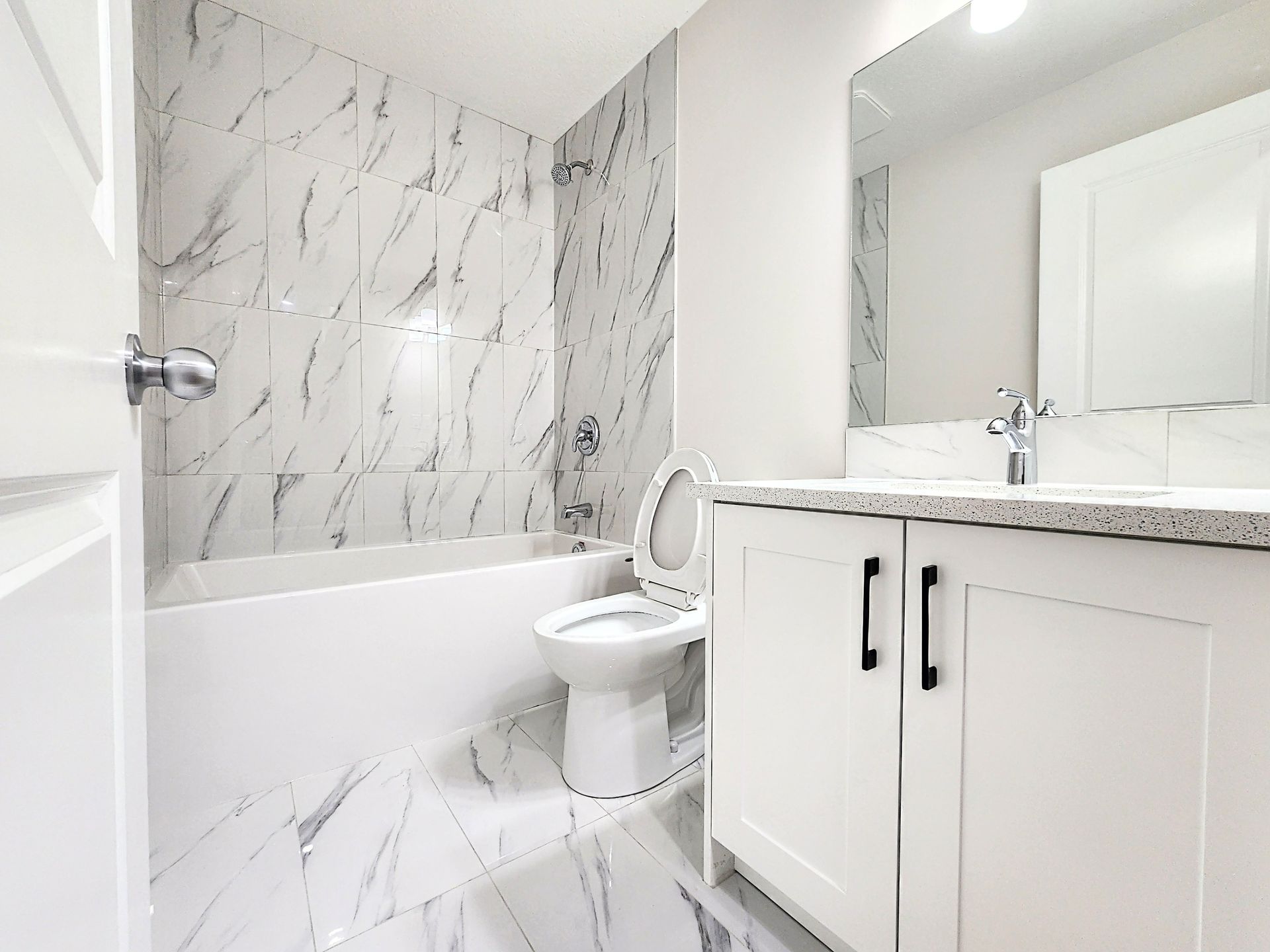 Bright bathroom with porcelain wall tiles, white bathtub, and vanity with Quartz countertop in a Calgary home's basement.