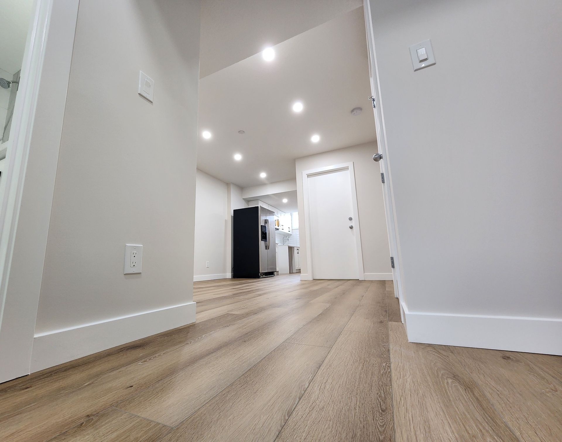 Low-angle view of a hallway with Vinyl flooring leading to a kitchen area in a newly developed Calgary basement.