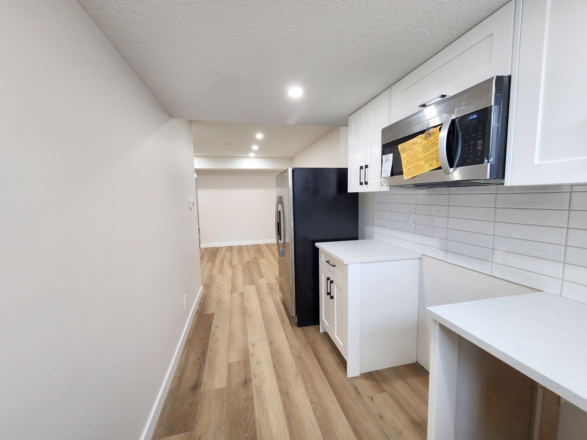 Modern kitchenette in a Calgary basement with stainless steel appliances, white cabinetry, and laminate flooring.