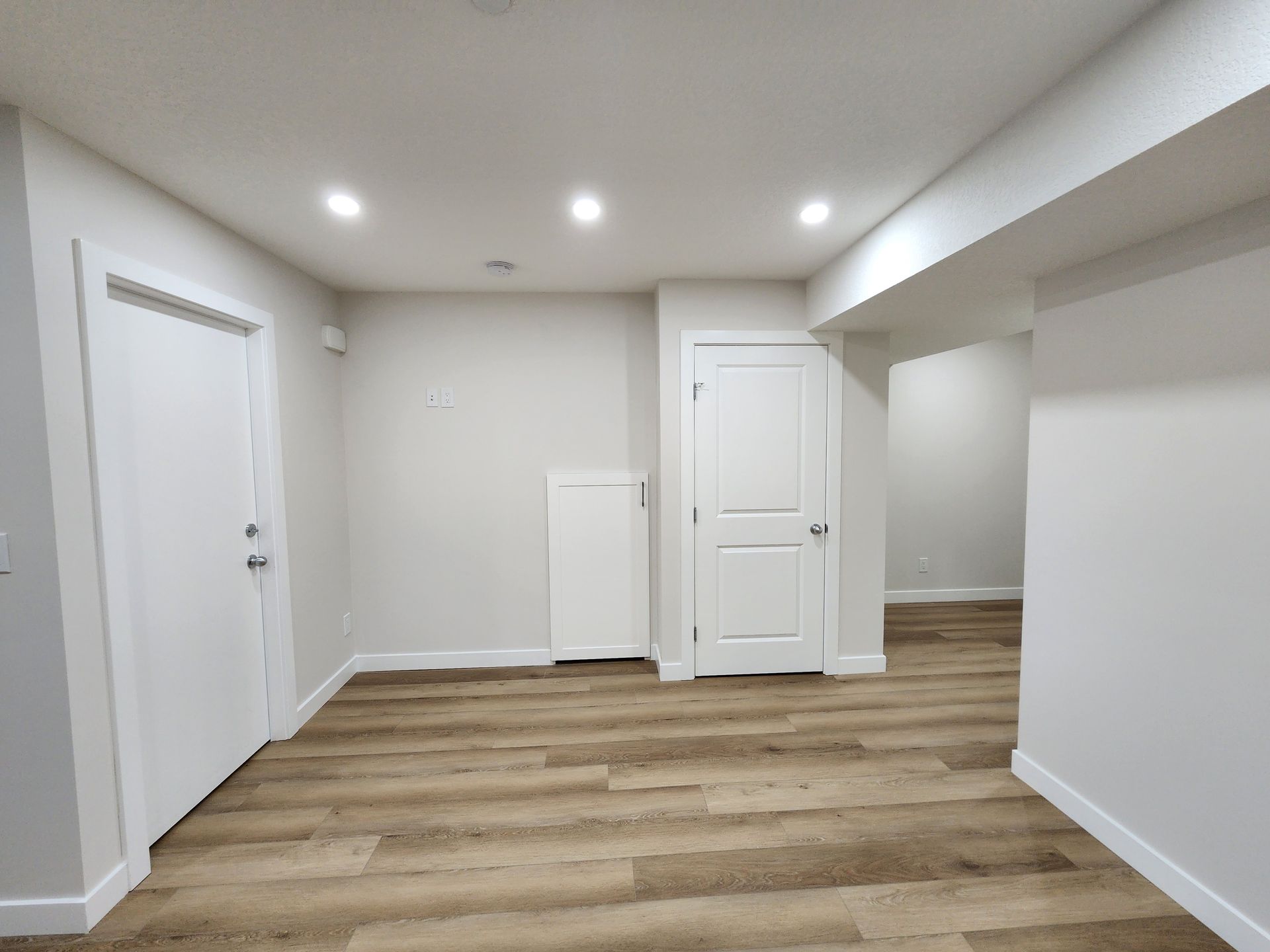 Open concept basement room with recessed lighting, Vinyl flooring, and white doors in a Calgary home.