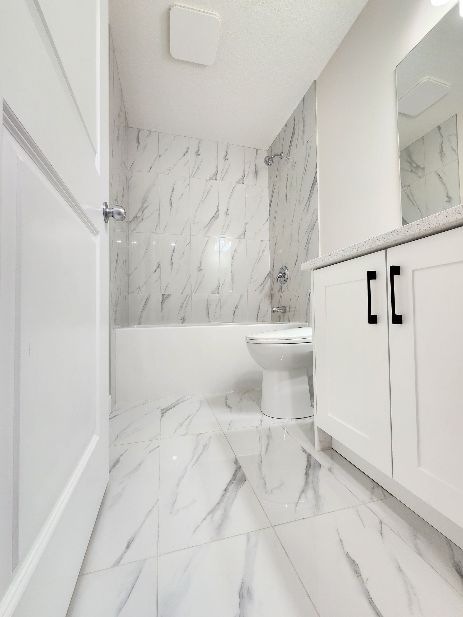 Elegant bathroom featuring marble tiles, a white vanity, and a wall-mounted toilet in a Calgary basement development.