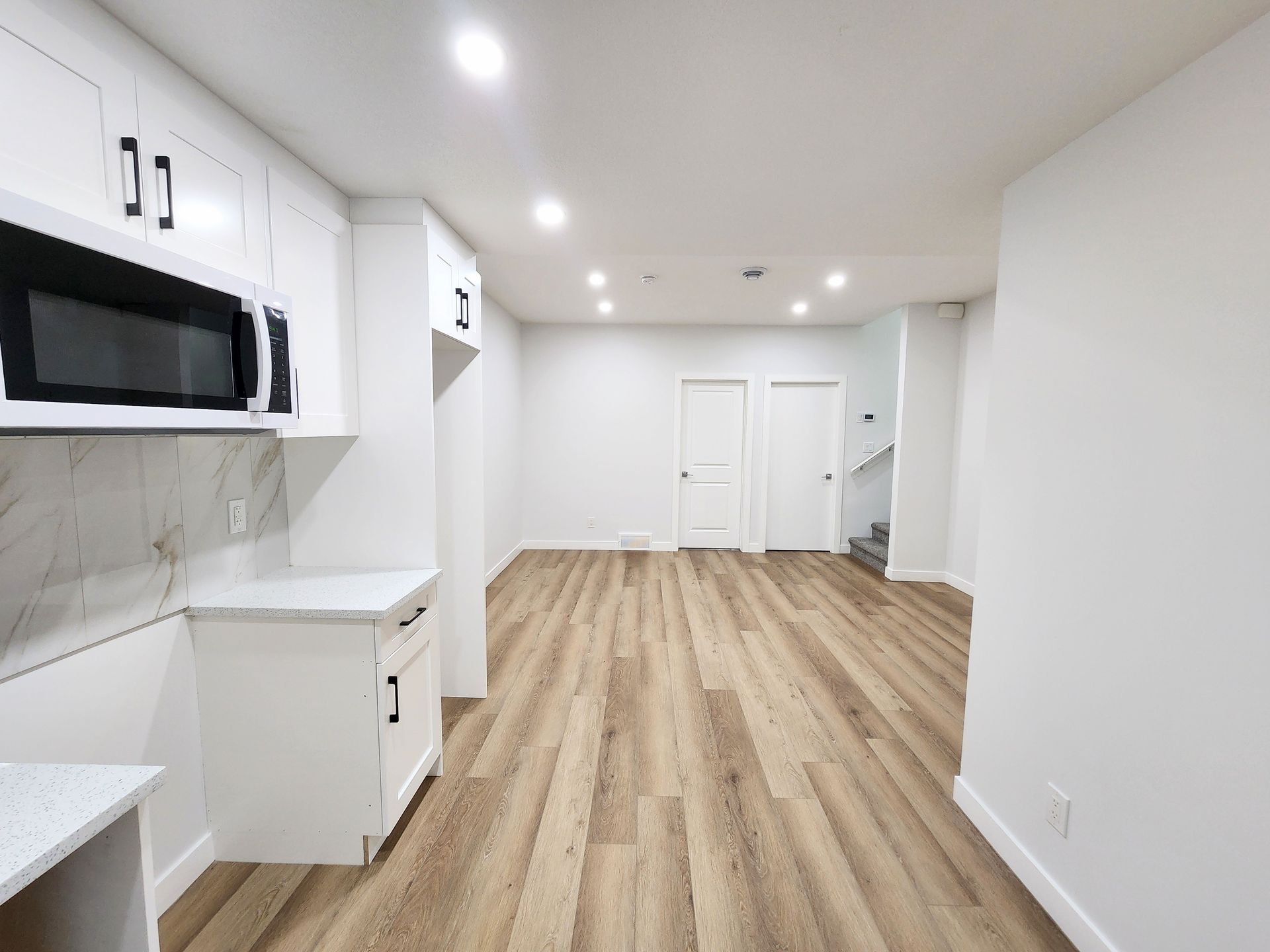 pictures shows a modern kitchen with white cabinets and microwave over a light wood floor in a basement development