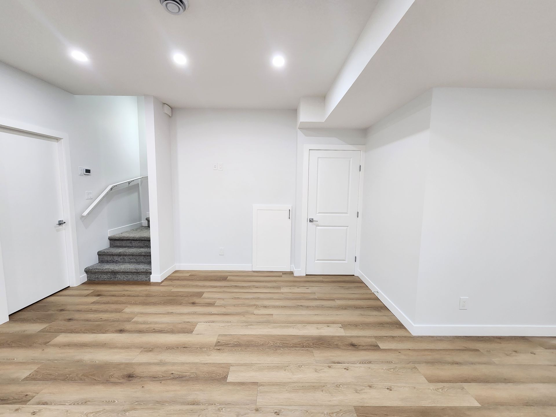 image shows spacious basement area with white walls and staircase within a basement renovation in Calgary