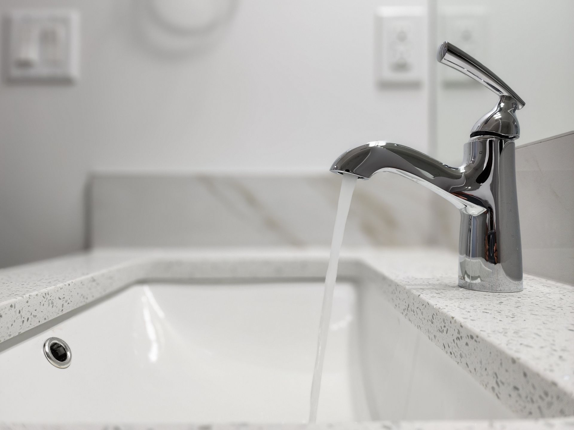 Sleek chrome bathroom faucet with running water over a white integrated sink in a Calgary home.