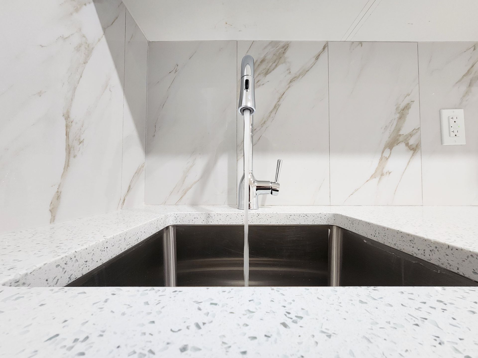 Kitchen sink with running water from a modern, chrome faucet against a marble backsplash in a Calgary residence