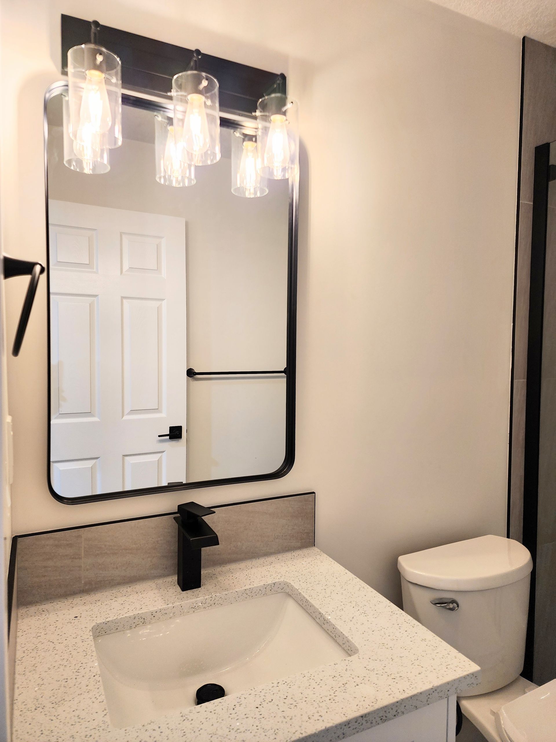 Image shows a black framed mirror and 3 light vanity fixture in a finished basement renovation in Calgary alberta