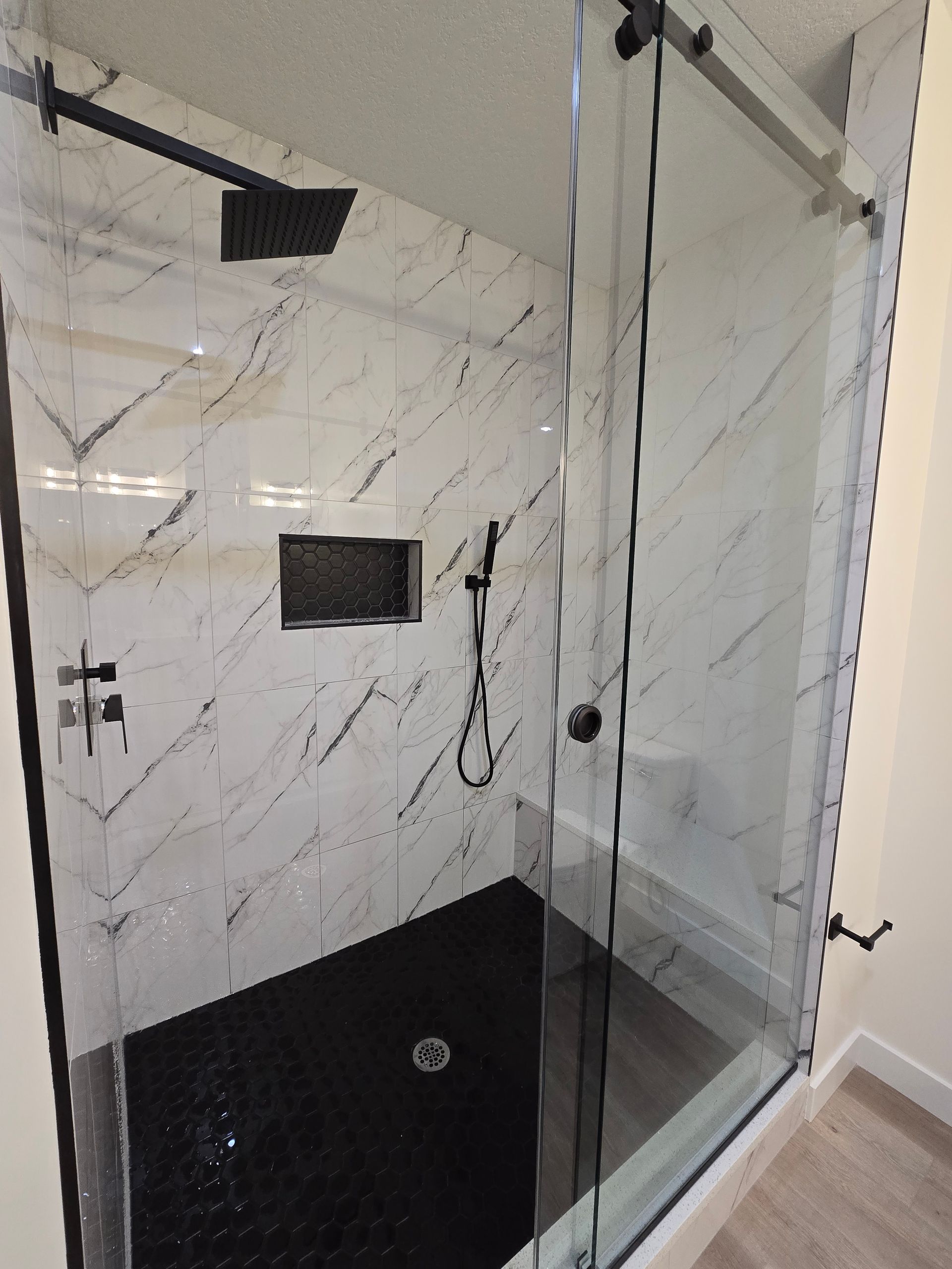 A luxury shower space with marble like tiles, black hardware's and a shower bench