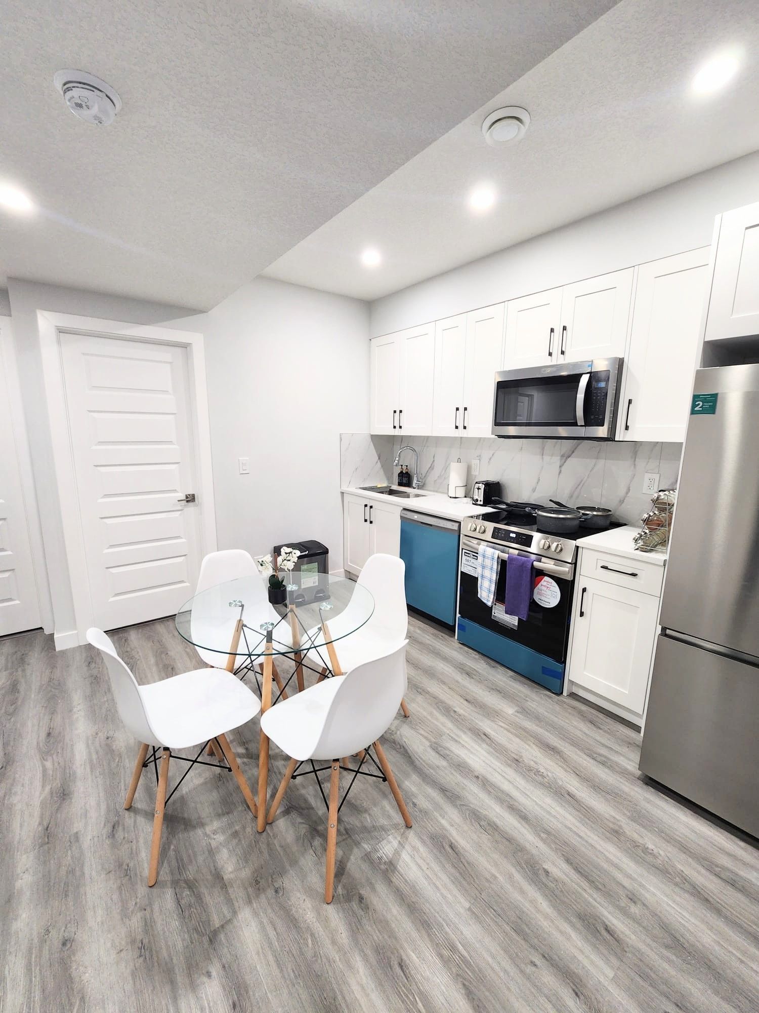 Image of white dinning chairs and round glass table in front of white kitchen within a basement suite in Calgary Alberta