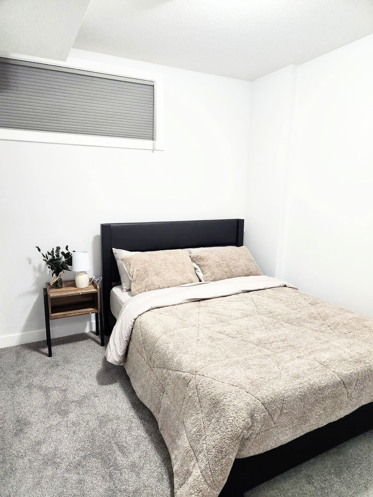 Picture of a queen bed and a side table in a bedroom of a finished basement in Calgary Alberta