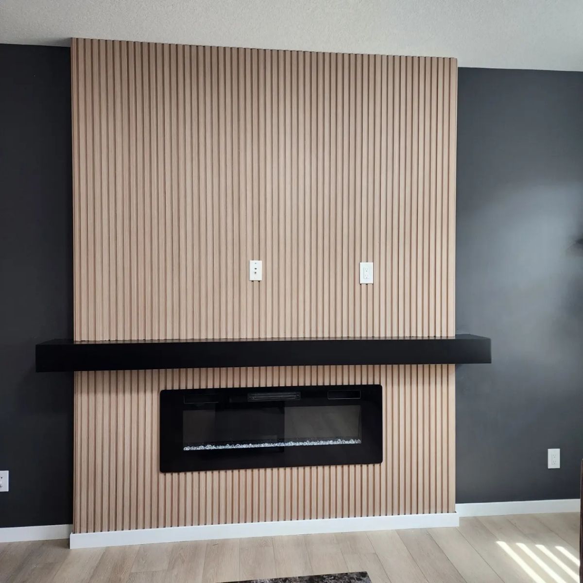 image shows a feature wall, with flutted oak panel, a black mantle and an electric fire place 