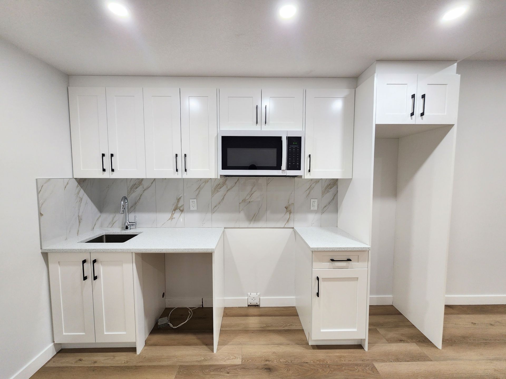 pictures shows compact kitchenette with white cabinetry and quartz countertops with a basement development in Calgary