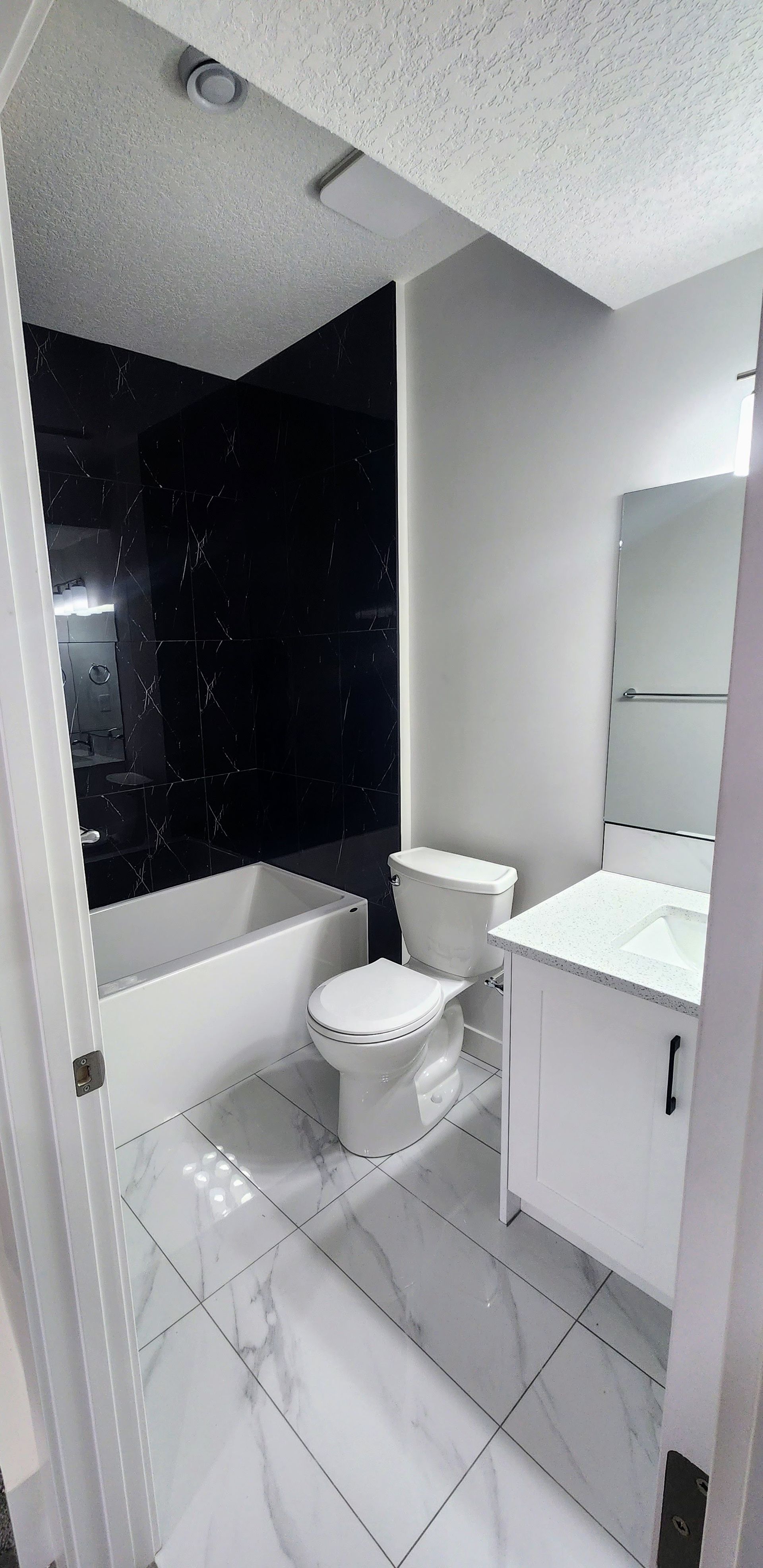 picture of a 3 piece bathroom, showing a white spec tiles, shaker style vanity and a toilet in Calgary basement development