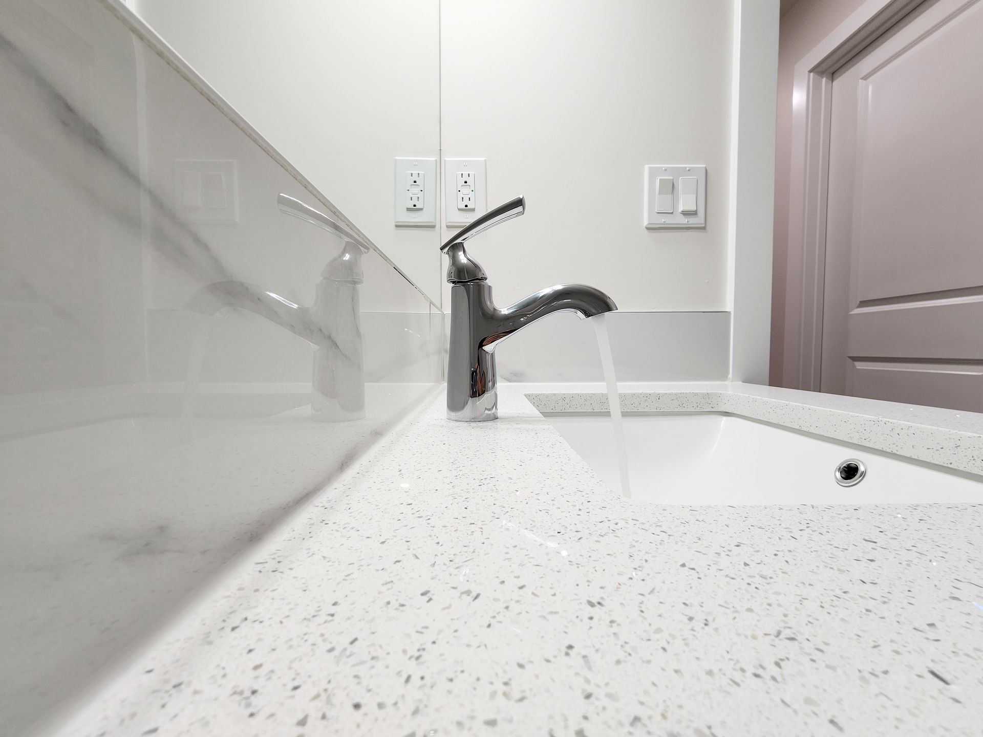 Bathroom sink withQuartz countertop and chrome faucet with running water in a newly developed Calgary basement.