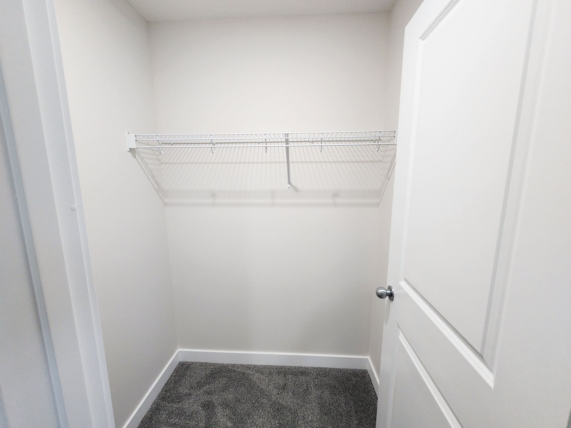 Pictures shows a basement closet with Free slide wire shelf, a grey carpeted floor and white wall in a Calgary basement development. 