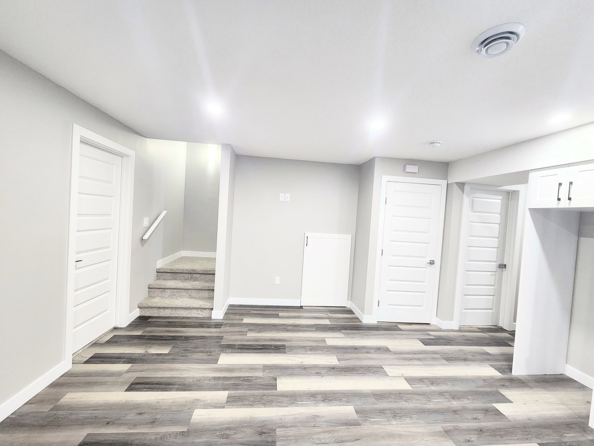 A basement area with a staircase on the left, multiple white doors, and a built-in countertop with cabinets.
