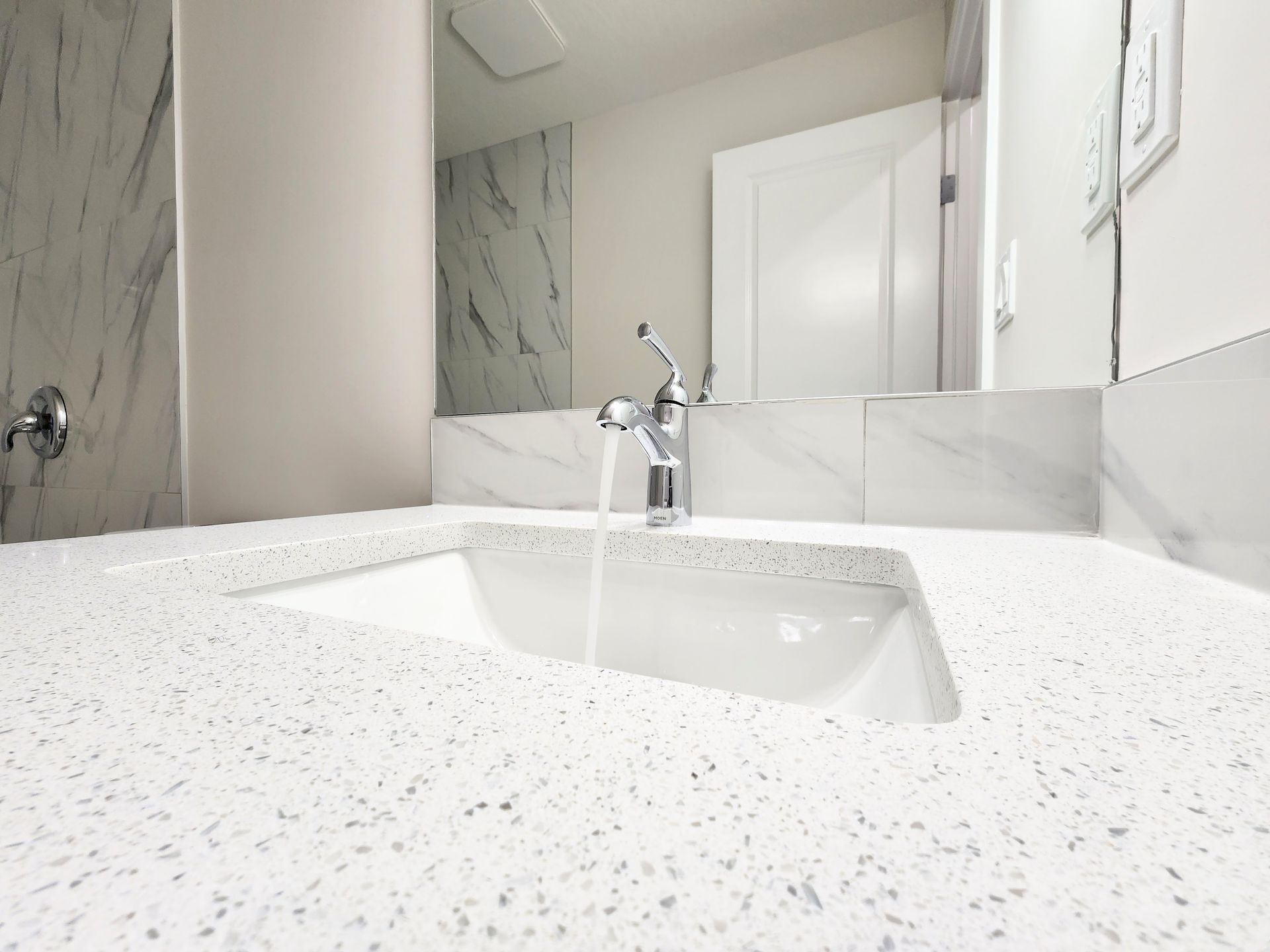 Bathroom sink withQuartz countertop and chrome faucet with running water in a newly developed Calgary basement.